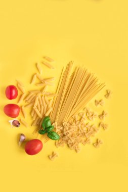 Fesleğen, domates ve sarı zemin üzerine sarımsak ile çeşitli pişmemiş çiğ makarna. İtalyan makarna: penne, farfalle, spagetti.
