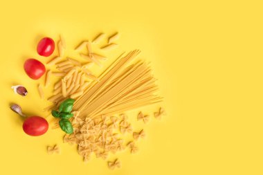 Fesleğen, domates ve sarı zemin üzerine sarımsak ile çeşitli pişmemiş çiğ makarna. İtalyan makarna: penne, farfalle, spagetti.