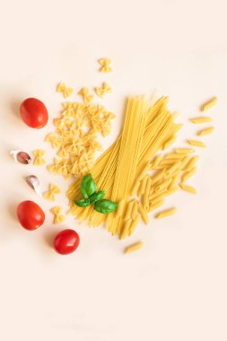 Fesleğen, domates ve sarımsak pastel pembe üzerinde çeşitli pişmemiş çiğ makarna. İtalyan makarna: penne, farfalle, spagetti.