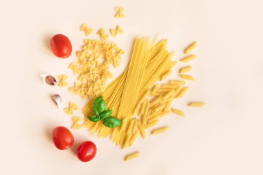 Fesleğen, domates ve sarımsak pastel pembe üzerinde çeşitli pişmemiş çiğ makarna. İtalyan makarna: penne, farfalle, spagetti.