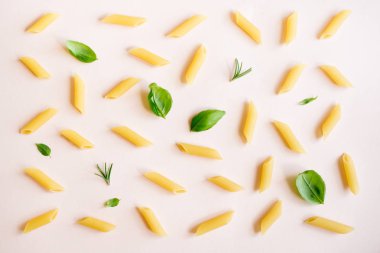 Penne makarna üzerine pastel pembe, en iyi görünüm, düz yatıyordu. Pişmemiş penne makarna otlar fesleğen ve biberiye ile desen.