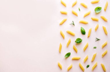 Penne makarna üzerine pastel pembe, en iyi görünüm, düz yatıyordu. Pişmemiş penne makarna otlar fesleğen ve biberiye ile desen.