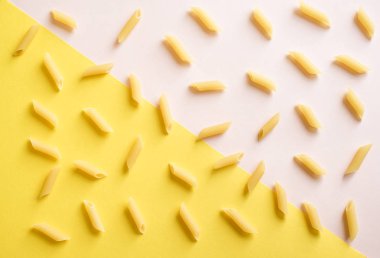 Düz penne makarna pembe pastel ve sarı arka plan, üstten görünüm üzerinde yatıyordu.