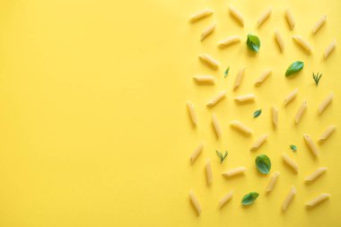 Sarı arka penne makarna en iyi görünüm, düz yatıyordu. Pişmemiş penne makarna otlar fesleğen ve biberiye ile desen.