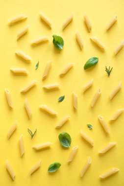 Sarı arka penne makarna en iyi görünüm, düz yatıyordu. Pişmemiş penne makarna otlar fesleğen ve biberiye ile desen.