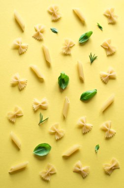 Penne ve Farfalle makarna üzerine sarı arka plan, üstten görünüm, lay düz. Fesleğen yaprakları ile çeşitli pasta kalıbı.