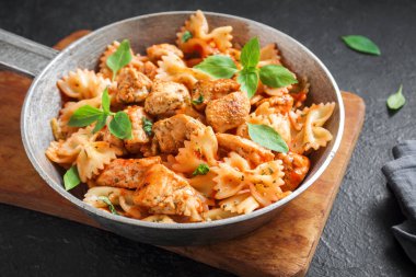 Farfalle makarna Tavuk ile domates sosu, fesleğen tavada. Tavuk İtalyan fiyonk makarna üzerine beton arka plan, ev yapımı Italyan Mutfagi.