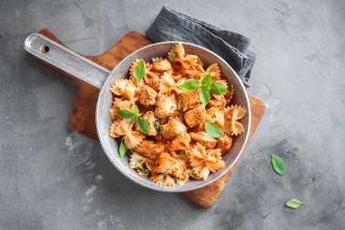 Farfalle makarna Tavuk ile domates sosu, fesleğen tavada. Tavuk İtalyan fiyonk makarna kopya alanı, ev yapımı İtalyan yemekleri ile beton arka plan üzerinde.