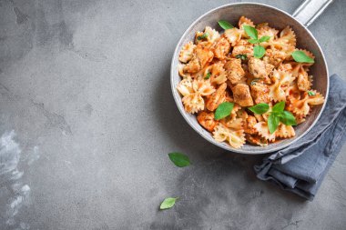 Farfalle makarna Tavuk ile domates sosu, fesleğen tavada. Tavuk İtalyan fiyonk makarna kopya alanı, ev yapımı İtalyan yemekleri ile beton arka plan üzerinde.