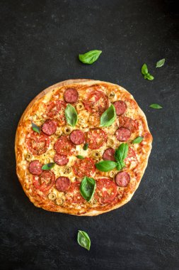 İtalyan Pizza domates, salam, yeşil zeytin, peynir ve fesleğen yaprakları, ana sayfa görünümü siyah. Taze ev yapımı Pizza, kopya alanı.