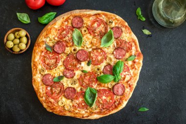 İtalyan Pizza domates, salam, yeşil zeytin, peynir ve fesleğen yaprakları, ana sayfa görünümü siyah. Taze ev yapımı Pizza, kopya alanı.