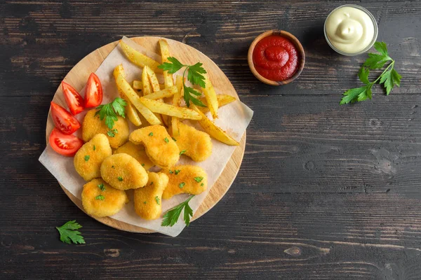 Tavuk nuggets, patates kızartması ve koyu ahşap arka plan, sosu alanı kopyalayın. Fried nuggets ve ketçap ve mayonez ile patates.