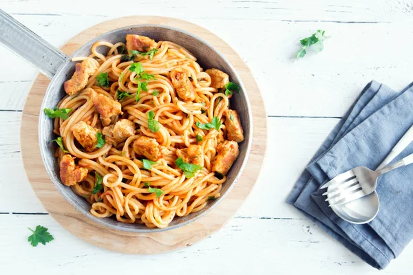 Spaghetti pasta in tomato sauce with chicken,  parsley in pan. Chicken spaghetti pasta over white wooden background with copy space, italian food.