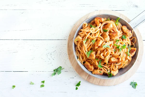 Spaghetti pasta in tomato sauce with chicken,  parsley in pan. Chicken spaghetti pasta over white wooden background with copy space, italian food.