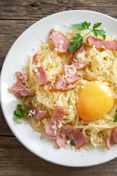 Spagetti carbonara Makarna yumurta sosu, pastırma ve rendelenmiş parmesan peynir - ev yapımı sağlıklı İtalyan makarna carbonara ahşap arka plan üzerinde