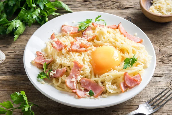 Spagetti carbonara Makarna yumurta sosu, pastırma ve rendelenmiş parmesan peynir - ev yapımı sağlıklı İtalyan makarna carbonara ahşap arka plan üzerinde