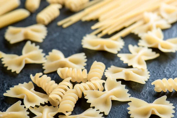 Assorted uncooked raw pasta on black background. Italian pasta: penne, farfalle, spaghetti, fusilli.