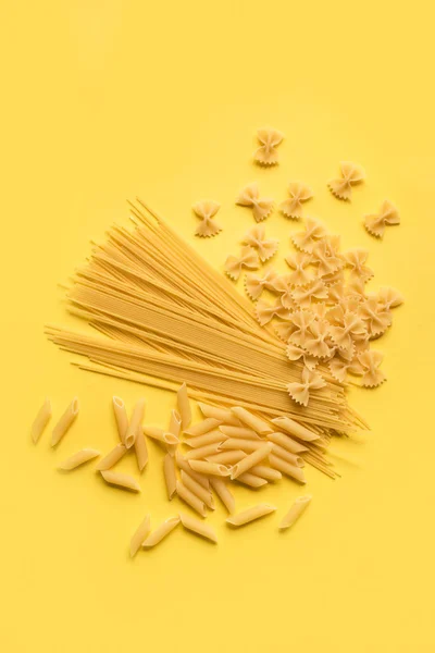 Assorted various uncooked raw pasta on yellow background. Italian pasta: penne, farfalle, spaghetti.