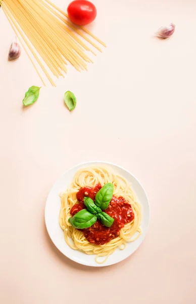 Spaghetti pasta bolognese and ingredients on pink background, top view. Plate of pasta dish with tomato sauce and basil, creative pastel background.