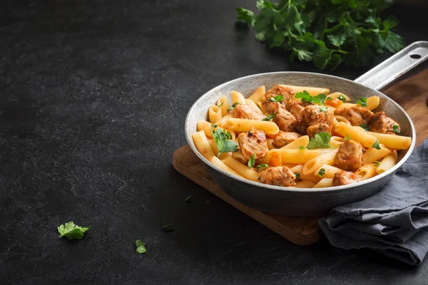 Penne pasta in tomato sauce with chicken,  parsley in pan. Chicken italian penne pasta over black background with copy space, italian food.