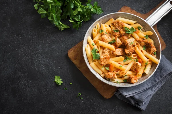 Penne pasta in tomato sauce with chicken,  parsley in pan. Chicken italian penne pasta over black background with copy space, italian food.