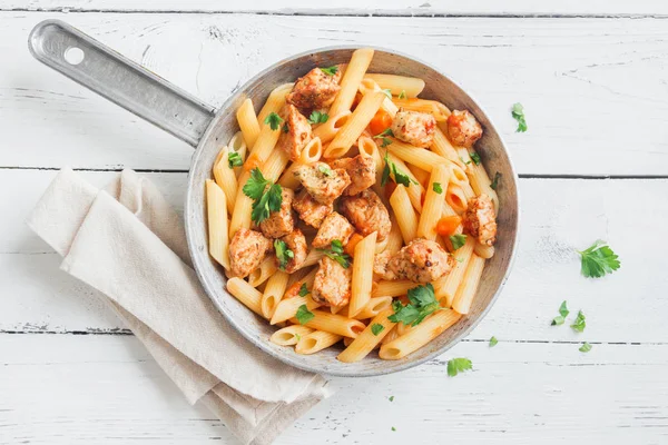 Penne pasta in tomato sauce with chicken,  parsley in pan. Chicken italian penne pasta over white background with copy space, italian food.
