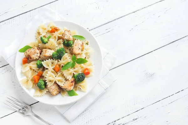 Farfalle pasta with chicken and vegetables. Pasta salad on white wooden background, copy space.