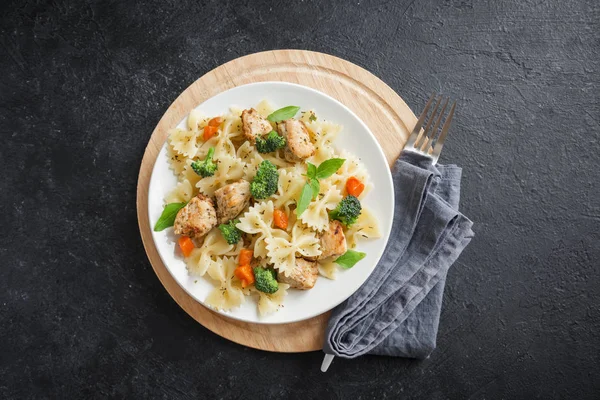 Farfalle pasta with chicken and vegetables. Pasta salad on black background, copy space.