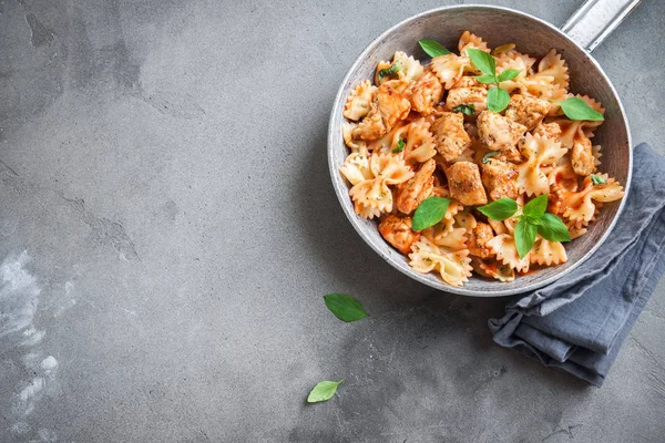 Farfalle makarna Tavuk ile domates sosu, fesleğen tavada. Tavuk İtalyan fiyonk makarna kopya alanı, ev yapımı İtalyan yemekleri ile beton arka plan üzerinde.