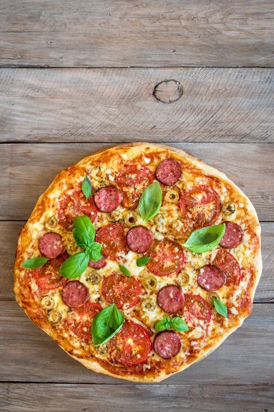 意大利比萨与西红柿 意大利腊肠 绿色橄榄 奶酪和罗勒叶子在木桌上 顶部的看法 新鲜自制比萨 复制空间 — 图库照片