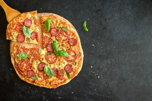  Dilim sucuk, domates, fesleğen, zeytin ve peynir ile İtalyan Pizza alarak. İtalyan Pizza ve Spatula kadar yakın siyah arka plan, üstten görünüm, kopya alanı üzerinde.