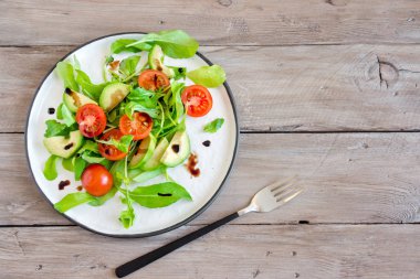 Roka ve ahşap üzerine balsamik sirke, kopya alanı ile avokado ve domates salatası. Sağlıklı beslenme vegan vejetaryen yaz sebze salatası gıda kavramı.