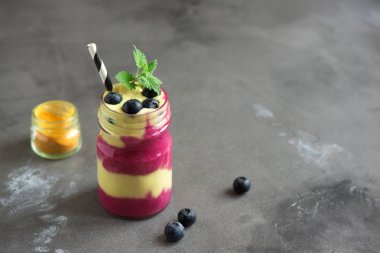 Yaban mersini ve zerdeçal güler yüzlü sağlıklı kahvaltı için. Karanlık beton zemin, kopya alanı üzerine çilek ile renkli katmanlı güler yüzlü.