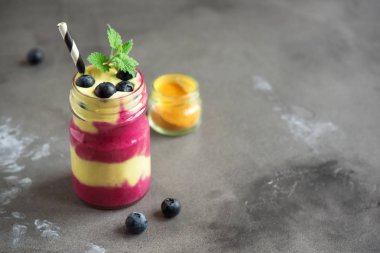 Yaban mersini ve zerdeçal güler yüzlü sağlıklı kahvaltı için. Karanlık beton zemin, kopya alanı üzerine çilek ile renkli katmanlı güler yüzlü.