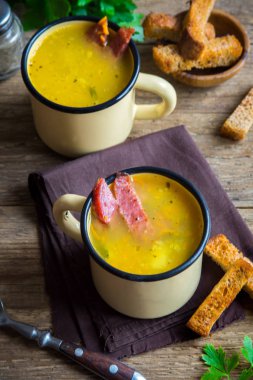 Bezelye çorbası ile jambon füme ve ahşap arka plan üzerinde kruton bölün. Kupalar kış öğle yemeği için sağlıklı ev yapımı kalın split çorba.
