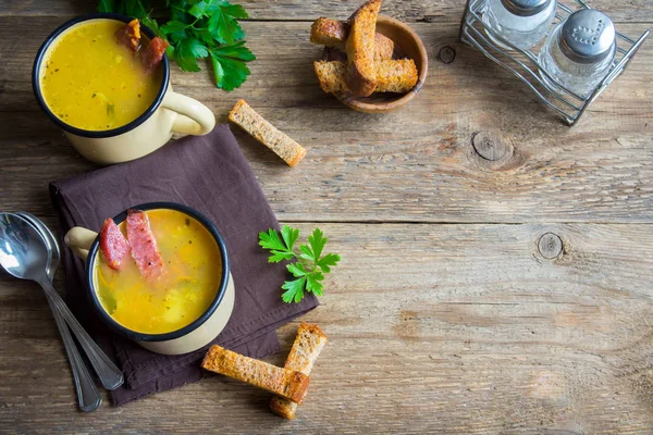 Bezelye çorbası ile jambon füme ve ahşap arka plan üzerinde kruton bölün. Kupalar kış öğle yemeği için sağlıklı ev yapımı kalın split çorba.