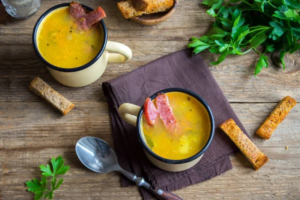 Bezelye çorbası ile jambon füme ve ahşap arka plan üzerinde kruton bölün. Kupalar kış öğle yemeği için sağlıklı ev yapımı kalın split çorba.