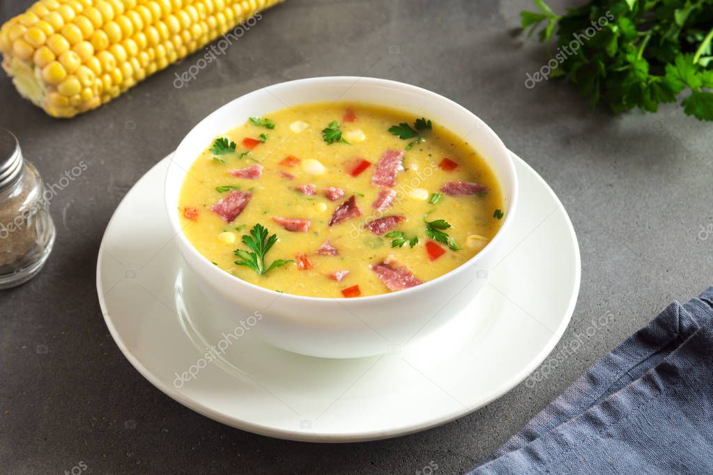 Homemade Corn Chowder Soup with Roasted Ham in white bowl. Healthy creamy corn soup with ham, greens and vegetables.