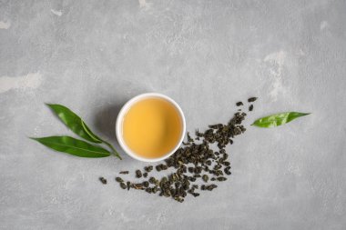 Yeşil çay seramik kupa, Kuru yeşil oolong çay ve çay yaprakları üstten görünüm, gri taş masada kopyalama alanı.