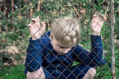 Üzgün, üzgün, oğlum sinirli (çocuk, çocuk, Genç) metal kafes, yakınındaki kapatın dikey, çocuk genç sorunları kavramı.