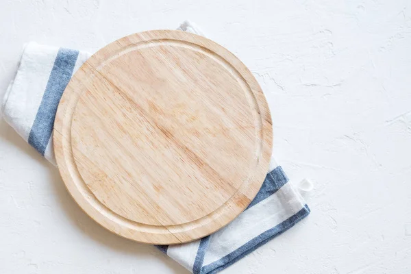 Empty wooden platter with napkin on white stone table, top view, copy space. Wooden cutting board over white concrete background.