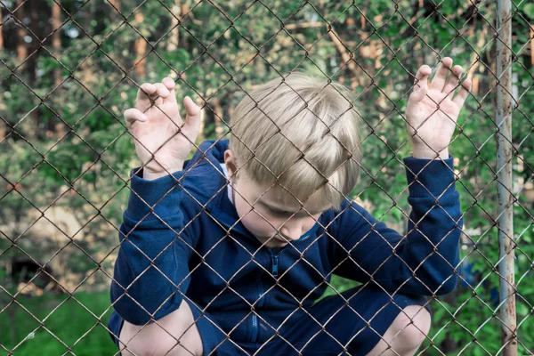 Üzgün, üzgün, oğlum sinirli (çocuk, çocuk, Genç) metal kafes, yakınındaki kapatın dikey, çocuk genç sorunları kavramı.