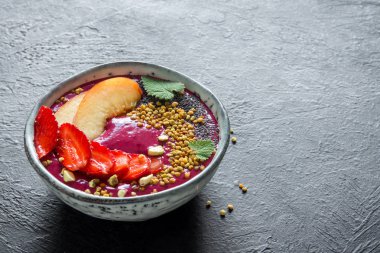 Acai smoothie kaseyle chia tohum, meyve, meyve (çilek) ve arı polen sağlıklı vegan vejetaryen diyet çiğ kahvaltı için. Siyah arka plan üzerine güler yüzlü kase kahvaltı.