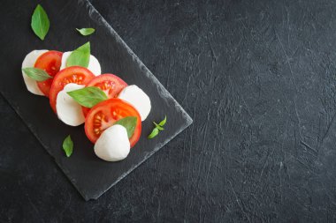 Geleneksel İtalyan Caprese salatası - dilimlenmiş domates, mozzarella peyniri ve fesleğen koyu taş arka plan, üstten görünüm, boşaltmak. Caprese salatası, İtalyan Akdeniz yemekleri.