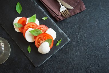Geleneksel İtalyan Caprese salatası - dilimlenmiş domates, mozzarella peyniri ve fesleğen koyu taş arka plan, üstten görünüm, boşaltmak. Caprese salatası, İtalyan Akdeniz yemekleri.