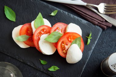 Geleneksel İtalyan Caprese salatası - dilimlenmiş domates, mozzarella peyniri ve fesleğen koyu taş arka plan, üstten görünüm, boşaltmak. Caprese salatası, İtalyan Akdeniz yemekleri.