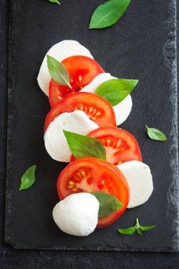 Geleneksel İtalyan Caprese salatası - dilimlenmiş domates, mozzarella peyniri ve fesleğen koyu taş arka plan, üstten görünüm, boşaltmak. Caprese salatası, İtalyan Akdeniz yemekleri.