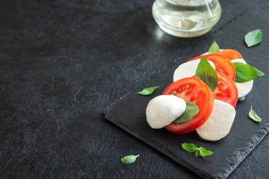 Geleneksel İtalyan Caprese salatası - dilimlenmiş domates, mozzarella peyniri ve fesleğen koyu taş arka plan, üstten görünüm, boşaltmak. Caprese salatası, İtalyan Akdeniz yemekleri.