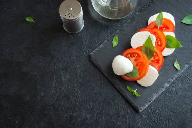 Geleneksel İtalyan Caprese salatası - dilimlenmiş domates, mozzarella peyniri ve fesleğen koyu taş arka plan, üstten görünüm, boşaltmak. Caprese salatası, İtalyan Akdeniz yemekleri.