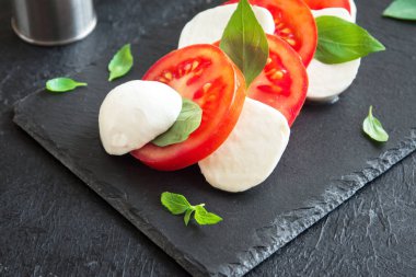 Geleneksel İtalyan Caprese salatası - taş koyu arka plan üzerinde dilimlenmiş domates, mozzarella peyniri ve fesleğen kapatın. Caprese salatası, İtalyan Akdeniz yemekleri.